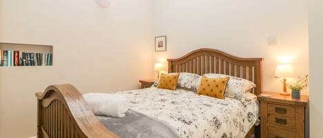 A bedroom with a wooden bed, two bedside tables with lamps, a bookshelf, and a ceiling light fixture.