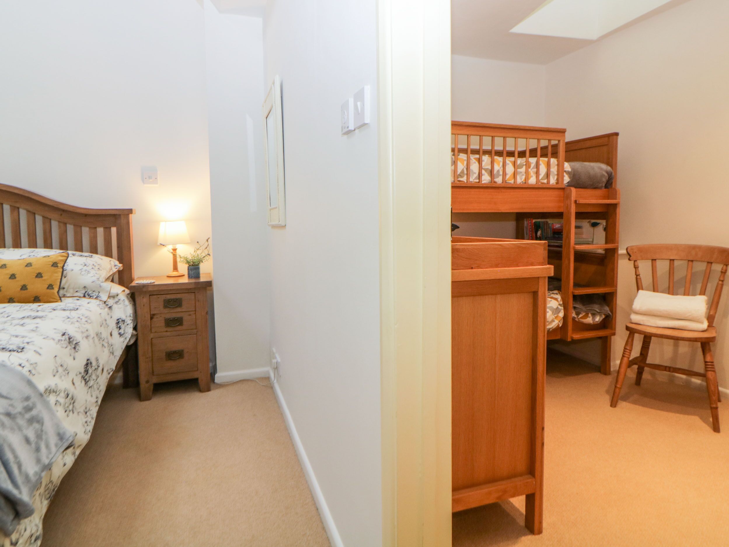 A bedroom with a bed, bedside table, lamp, and a wooden shelf unit with a chair.