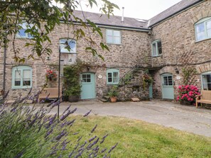 A stone building with multiple windows and doors, some with flower boxes. There is a bench and a potted plant in the foreground. - Blackberry Cottage (Kingsbridge)