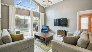 A living room with a sofa, armchair, coffee table, TV, and a sliding glass door leading to a balcony.