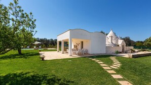 Una casa moderna con una torre de piedra, un patio con mobiliario exterior y un césped bien cuidado.