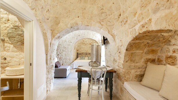 Una habitación con paredes de piedra, una cama, una mesa de comedor con sillas y un sofá.