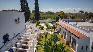 A residential area with a white building, a covered outdoor seating area, and a garden with various plants. - 3367 Villa Parco Grande by Perle di Puglia (Carovigno)