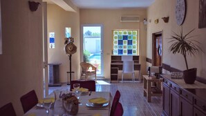 A dining area with a table set for four, a wicker chair, a potted plant, and a wall clock. - 3367 Villa Parco Grande by Perle di Puglia (Carovigno)