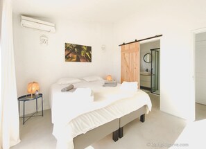 Una camera da letto con un letto, lampade da comodino, un condizionatore d'aria a parete, un quadro e un bagno con porta in vetro.