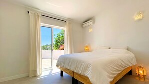 Een slaapkamer met een groot bed, een schuifpui naar een balkon, een wandairconditioner en twee wandlampen.