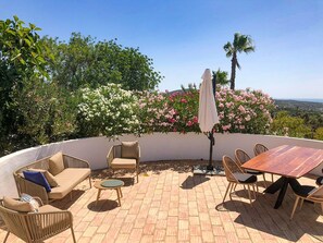 Una terrazza esterna con una zona salotto a forma di curva, un tavolo rotondo e vista sul paesaggio.