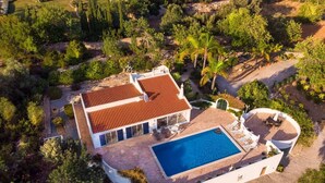 Luchtbeeld van een modern huis met een zwembad, omringd door weelderige begroeiing en palmbomen.