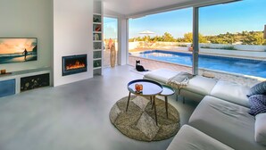 Een moderne woonkamer met een open haard, uitzicht op een zwembad en een comfortabele zithoek.