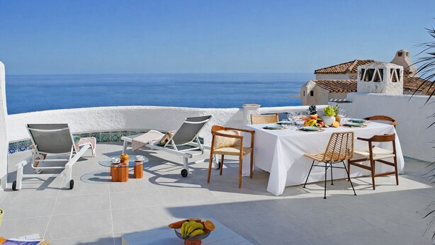Una terrazza con un tavolo apparecchiato per mangiare, poltrona lounge e vista sul mare.