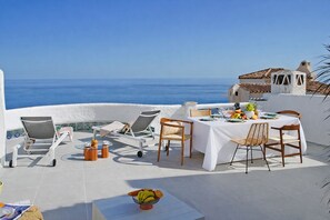 A terrace with a table set for dining, lounge chairs, and a view of the sea. - Comeback La Casa del Sol Naciente (Salobreña)