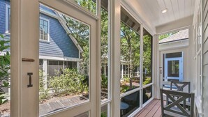 A covered porch with large windows, a wooden deck, and a view of a house with a blue roof.