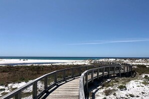 Una passerella in legno che conduce a una spiaggia con dune e un cielo sereno.