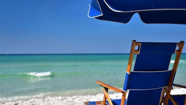 A beach chair and umbrella on a sandy beach with clear turquoise water and a clear sky.