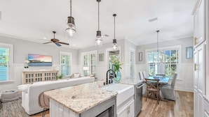 A modern kitchen with a central island, pendant lighting, and a dining area with a table and chairs.