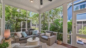 A covered patio with wicker furniture, a ceiling fan, and a view of the surrounding greenery.