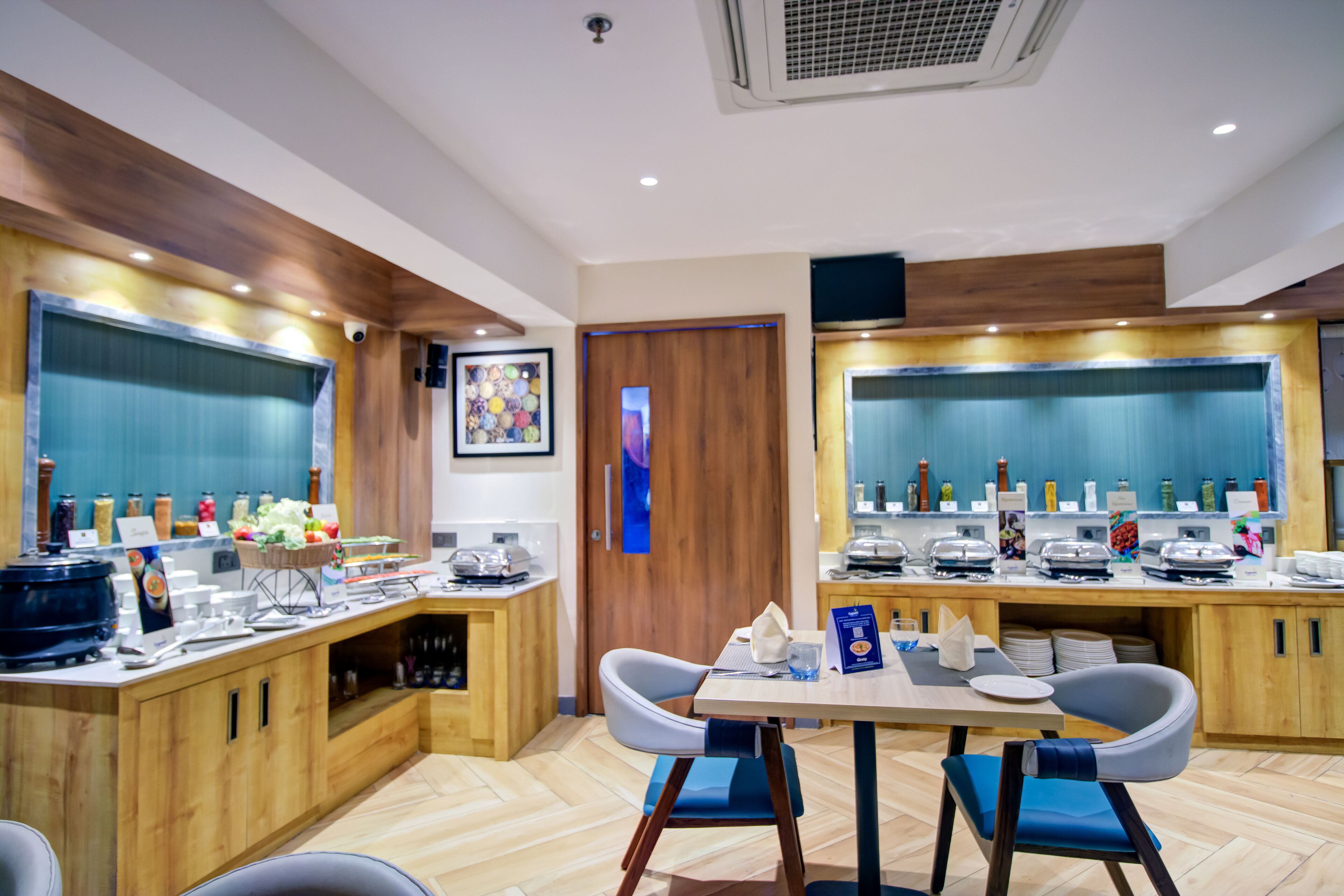 Un comedor de hotel moderno con armarios de madera, un sistema de buffet y un arreglo de asientos con sillas azules.