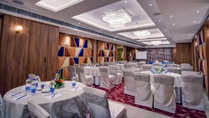 Un salón de conferencias con mesas redondas, sillas blancas y una alfombra roja.