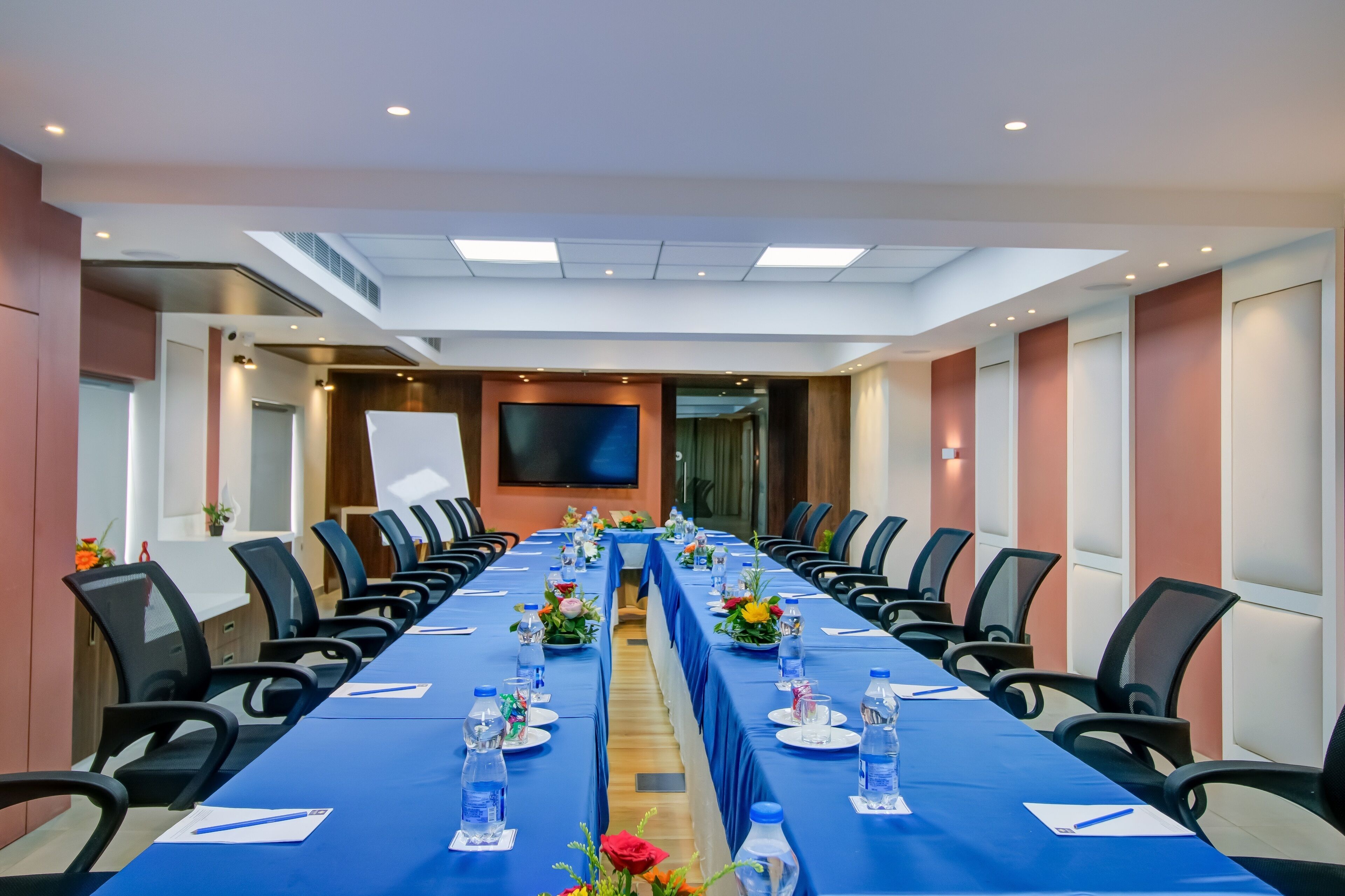 A conference room with a long table, chairs, and a large screen.