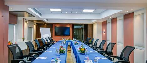 A conference room with a long table, chairs, and a large screen.
