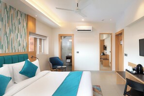 Habitación de hotel con cama, escritorio, silla, mesita pequeña, televisor y aire acondicionado.