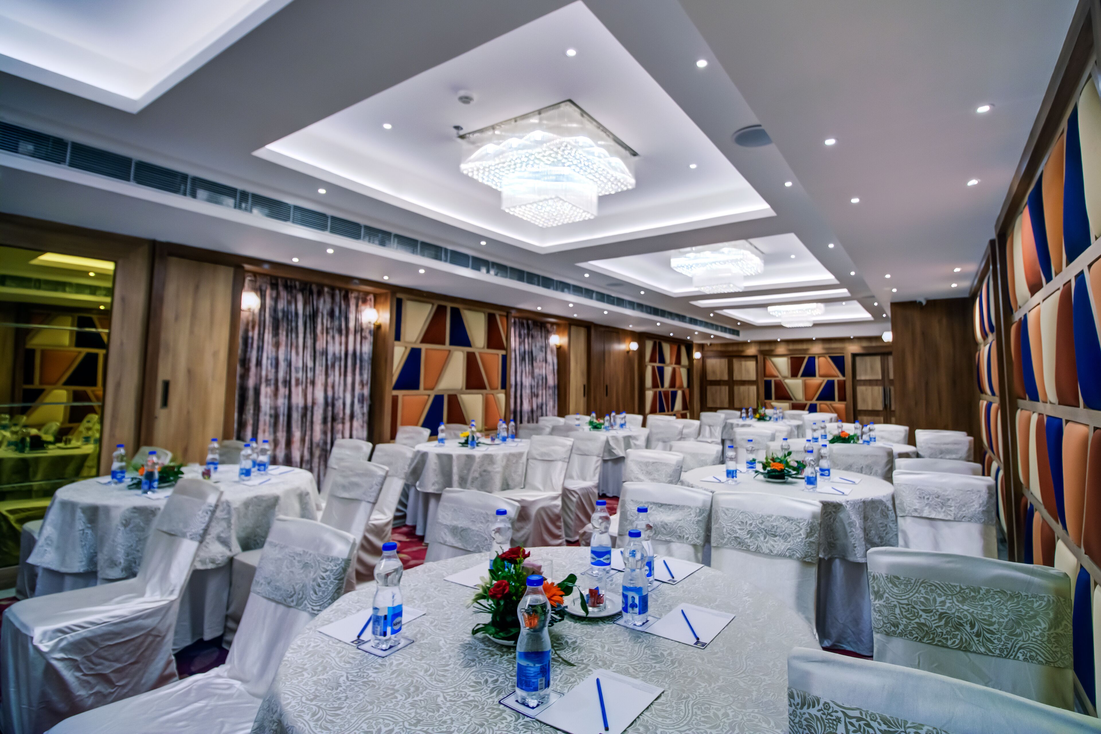Un salón de banquetes con mesas redondas, manteles blancos y sillas cubiertas de blanco.