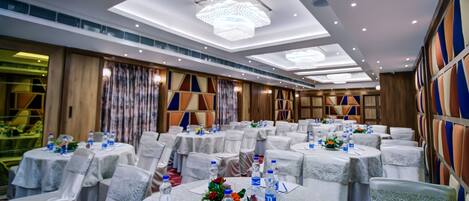 Un salón de banquetes con mesas redondas, manteles blancos y sillas cubiertas de blanco.