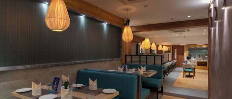 Een restaurant met smaragdgroene banken, houten tafels en hanglampen.