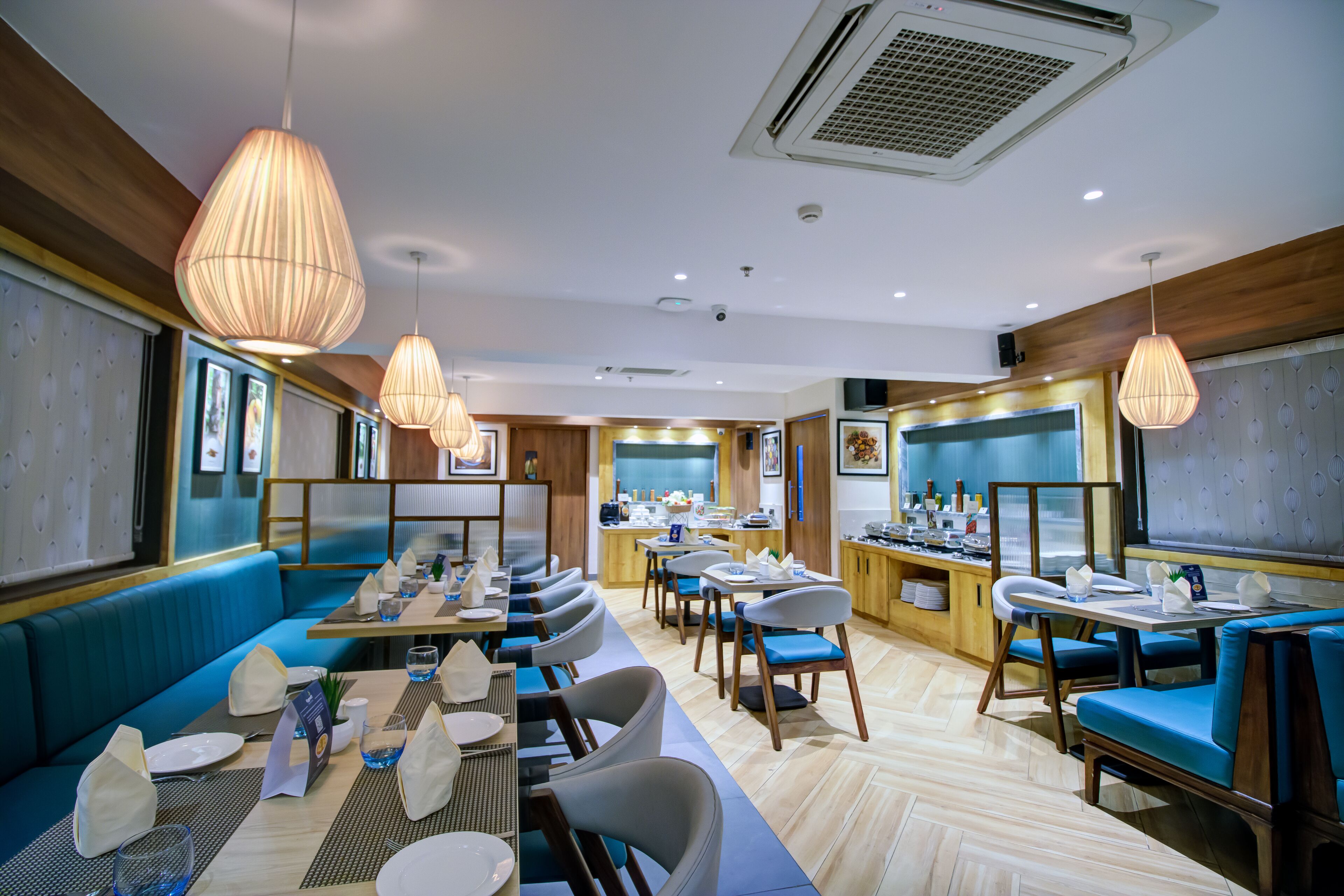 Un restaurante con asientos y mesas azules, lámparas colgantes y una zona de cocina al fondo.
