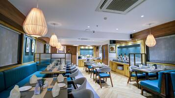 A restaurant with blue booths and tables, hanging pendant lights, and a kitchen area in the background.