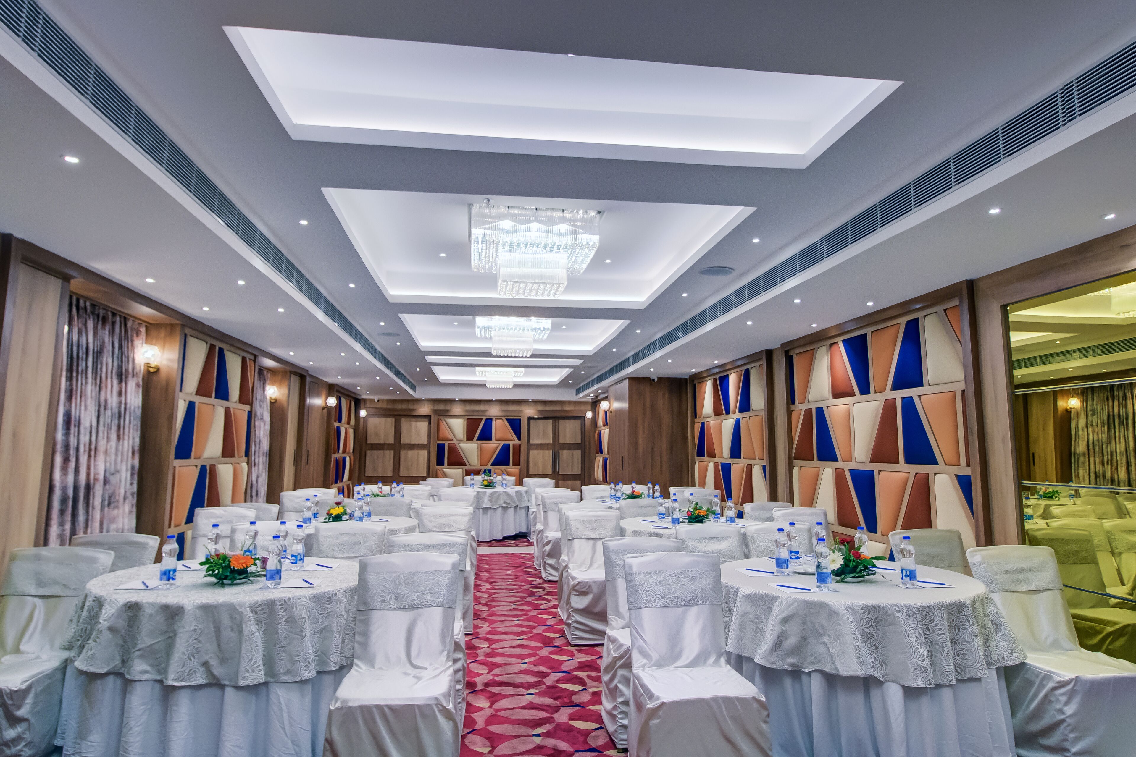 Un salón de banquetes con mesas redondas, sillas blancas y un pasillo central.