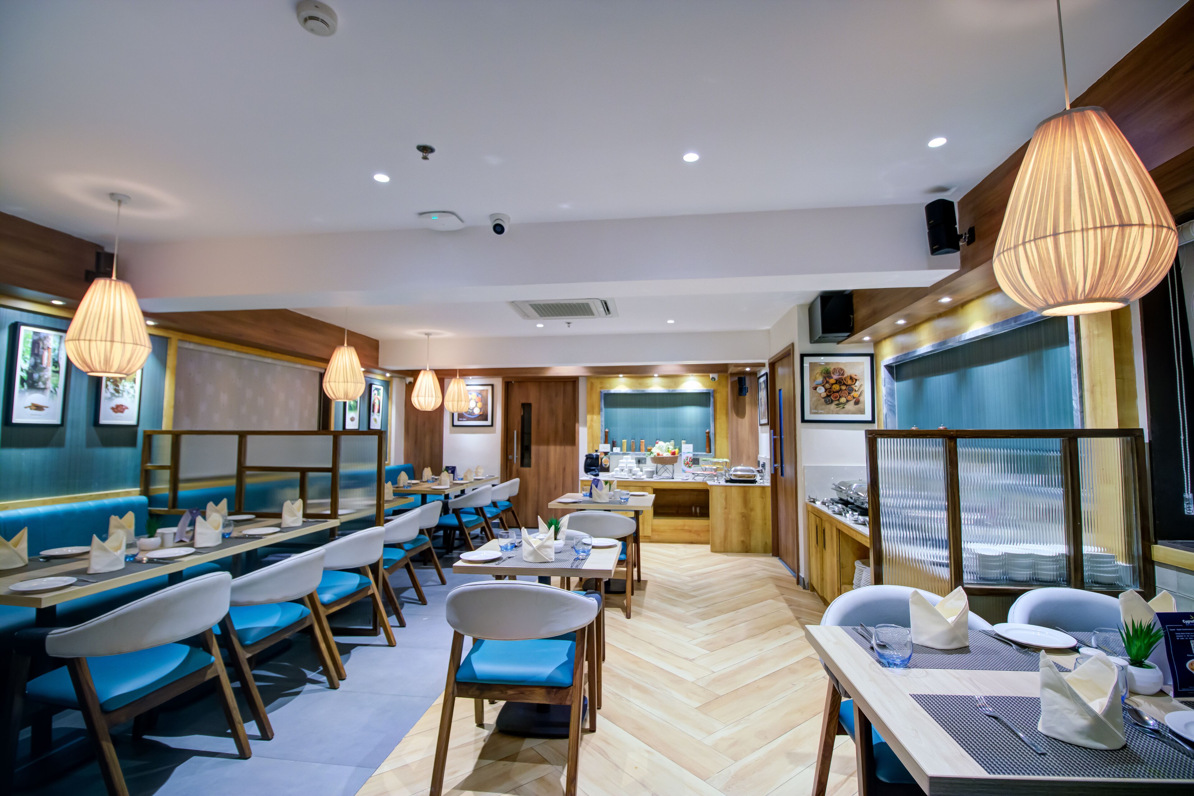A restaurant with wooden flooring, blue cushioned booths, and hanging pendant lights.