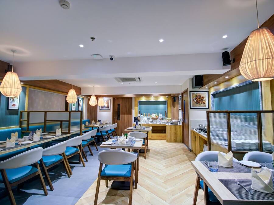 A restaurant with wooden flooring, blue cushioned booths, and hanging pendant lights.