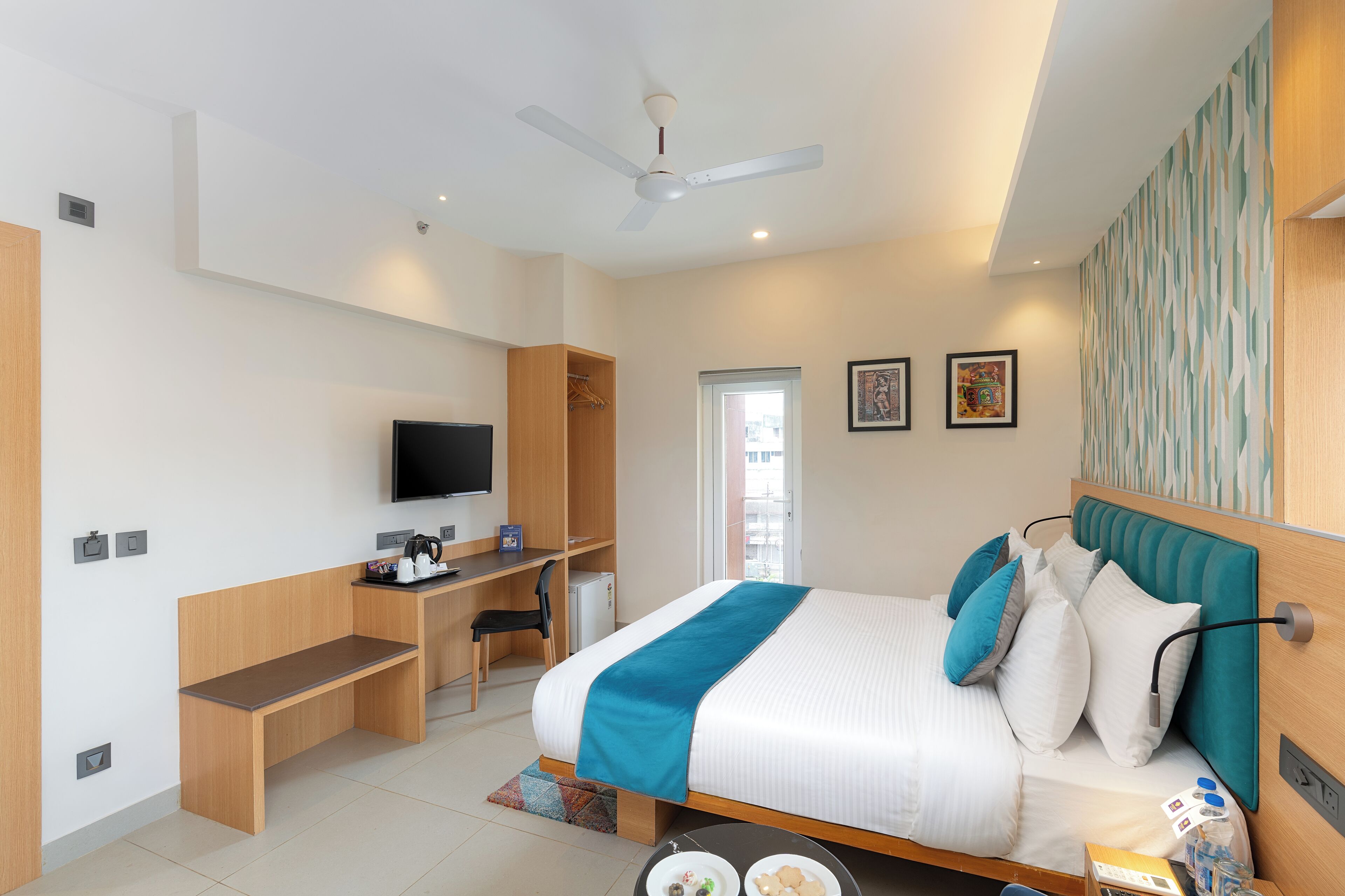 A modern hotel room with a bed, desk, chair, TV, and a ceiling fan.