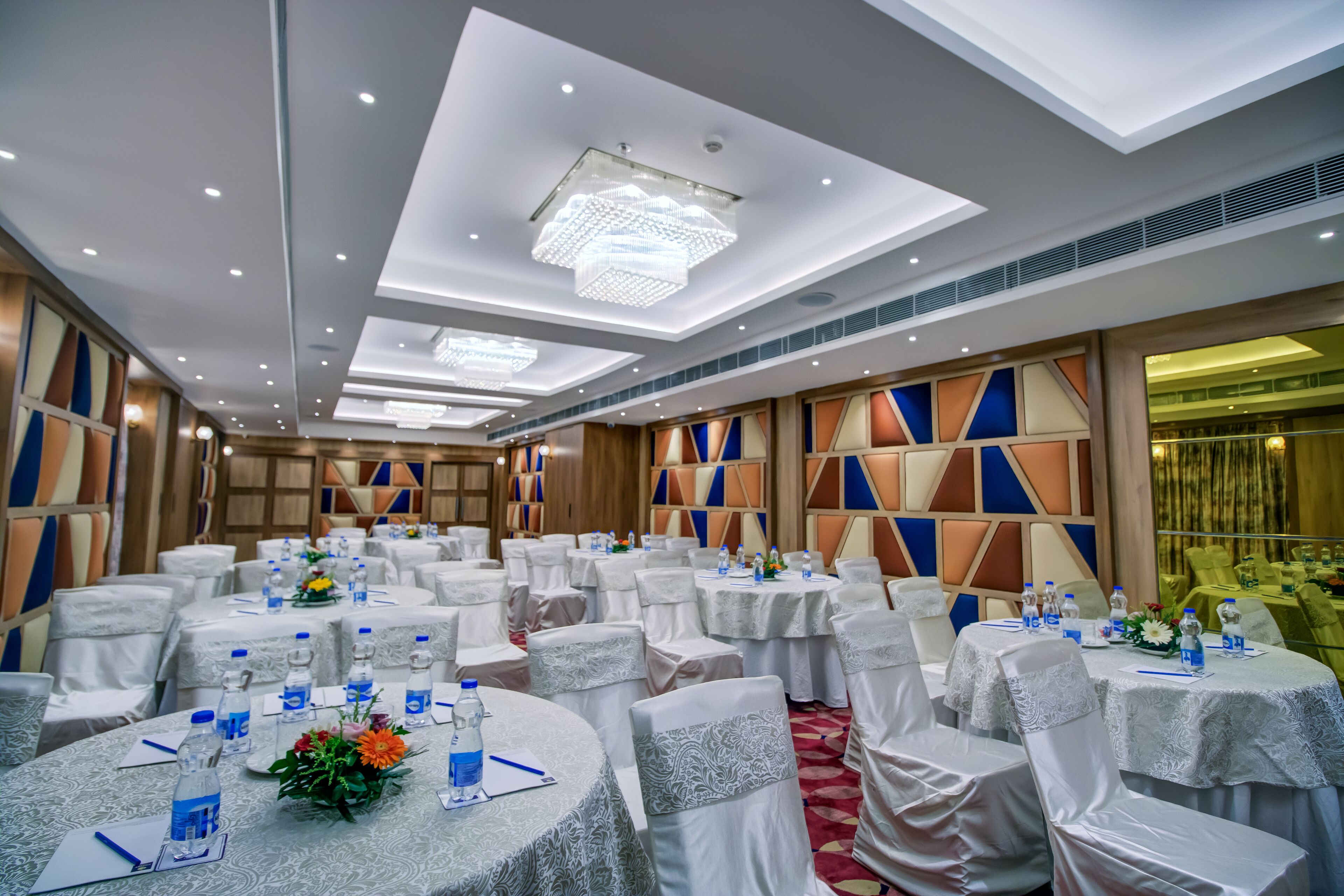 A banquet hall with round tables, white tablecloths, and chairs with white covers.