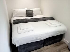A neatly made bed with white linens, a dark gray throw blanket, and two folded white towels. - Rural Apartment in Rural Wroxford Near Banbury (Banbury)