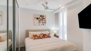 Een moderne slaapkamer met een bed, een plafondventilator, een schilderij en een televisie.