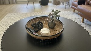 Uma mesa redonda com um tabuleiro de palha, um vaso pequeno com uma planta e uma vela.