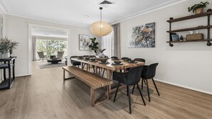 Uma sala de jantar moderna com uma mesa de madeira comprida, cadeiras pretas e um lustre.