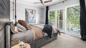 Quarto com cama grande, ventoinha no teto, janela com vista para o verde e um quadro na parede.