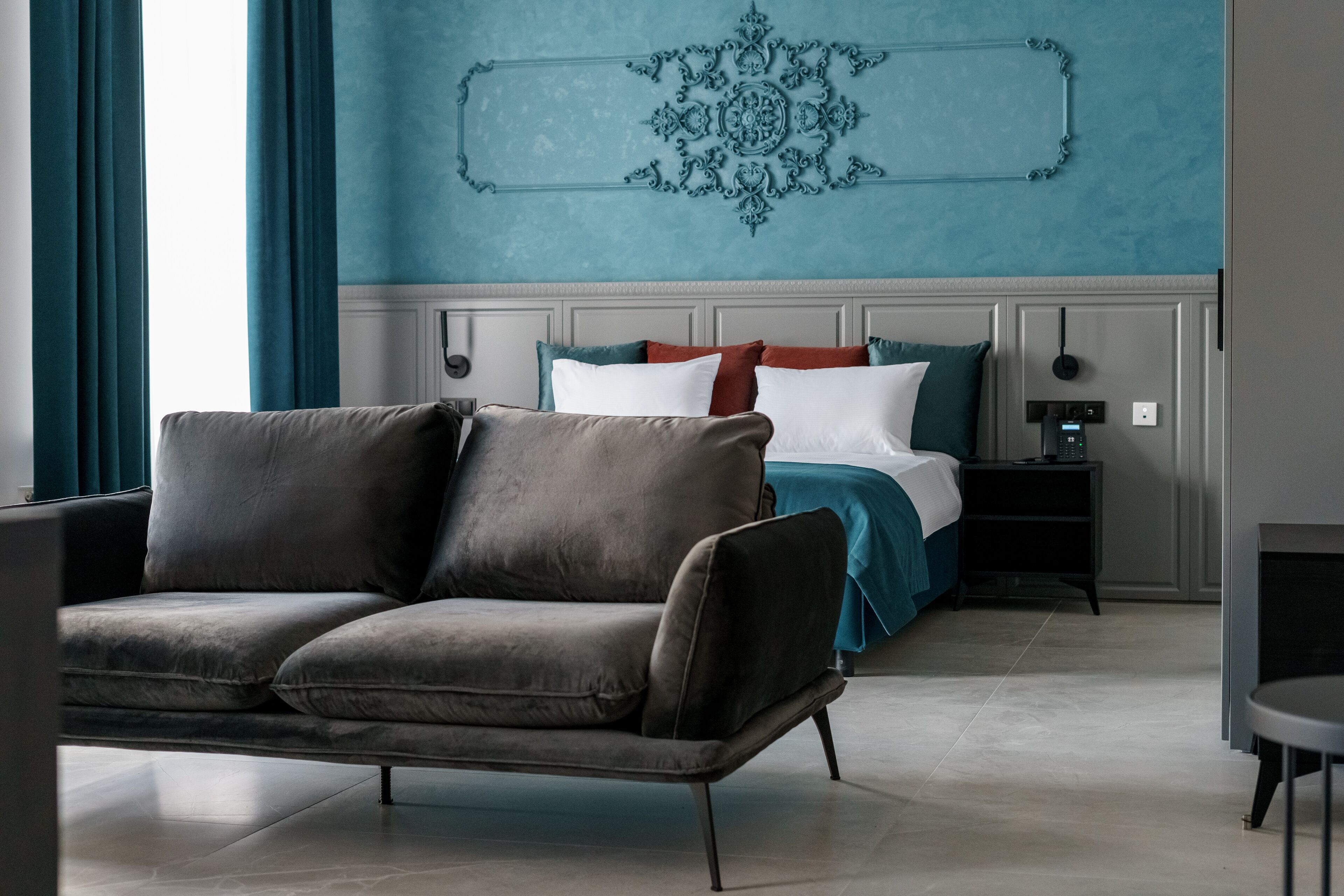 A modern bedroom with a grey sofa, a bed with teal and white bedding, and a decorative wall piece.