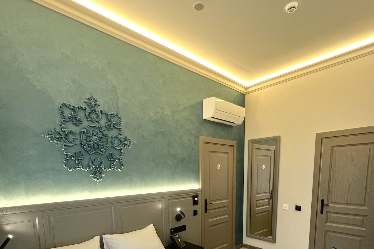 A hotel room with a bed, bedside table, and a wall-mounted air conditioning unit.