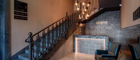 A staircase with a metal railing leading to a reception area with a marble counter and blue chairs.