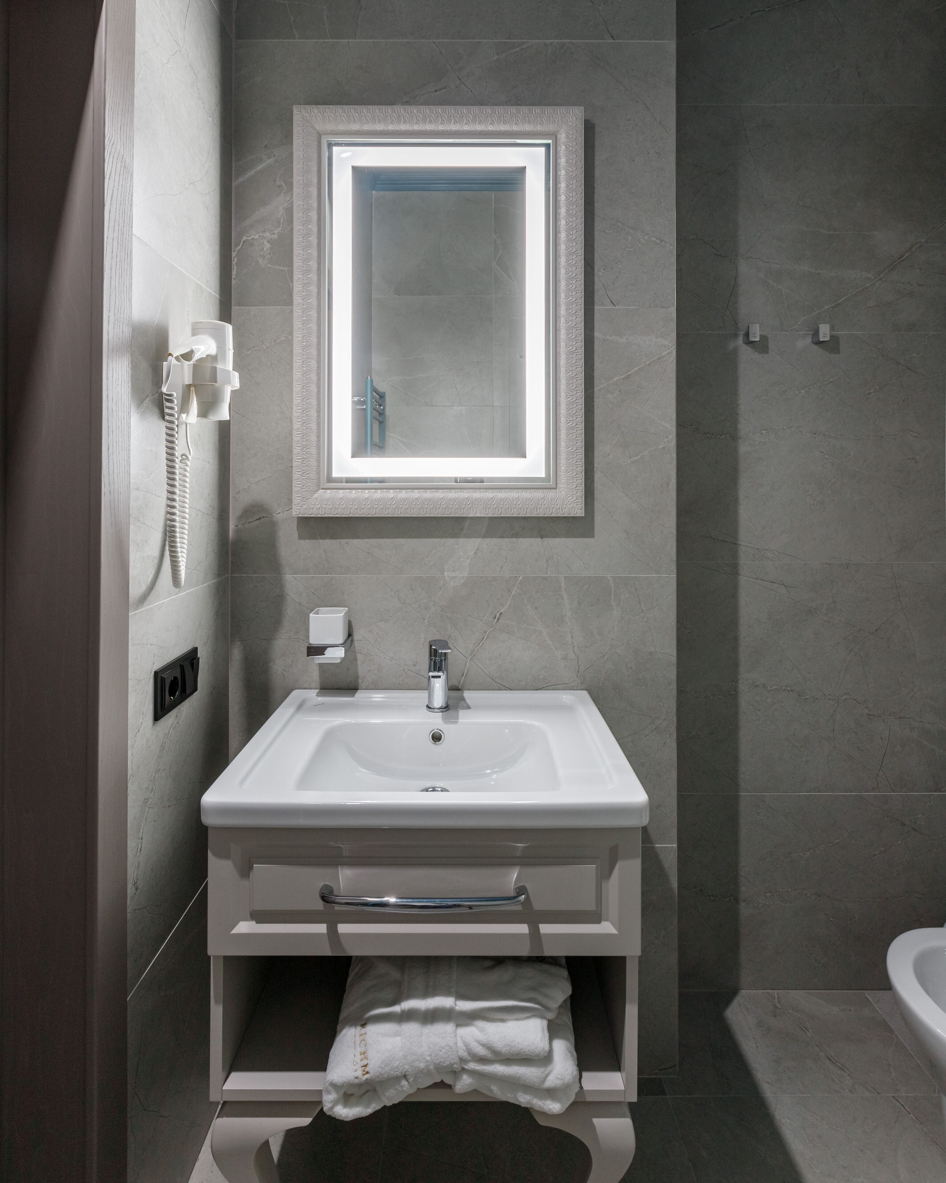 A modern bathroom with a large rectangular sink, a mirror with a decorative frame, a towel rack, and a handheld showerhead.