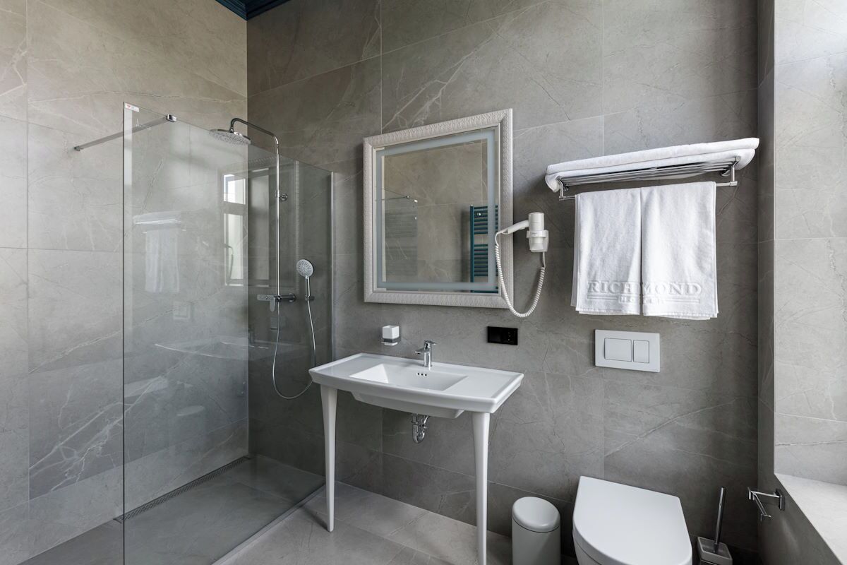 A modern bathroom with a glass-enclosed shower, a white sink, a toilet, and a towel rack.
