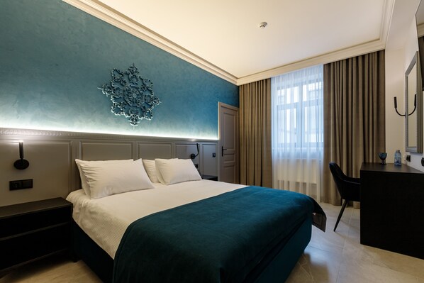 A hotel room with a bed, a desk, a chair, a nightstand, and a decorative wall piece. - Richmond Hotel (Chisinau)