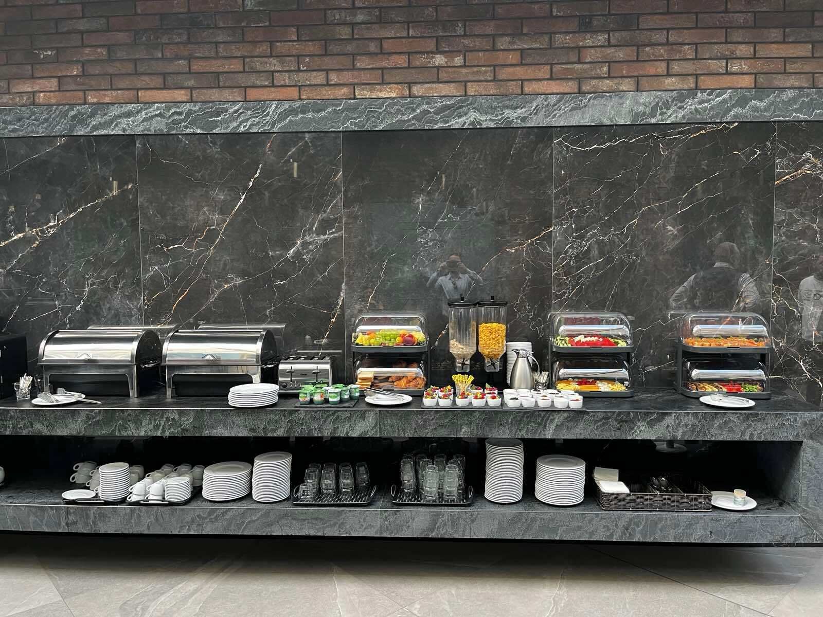 En buffetopstilling med forskellige madstationer, herunder grill, frugt og salat.