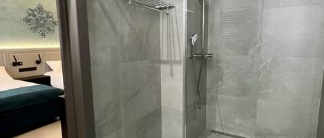 A modern bathroom with a shower, a towel rack, and a bed in the adjacent room.