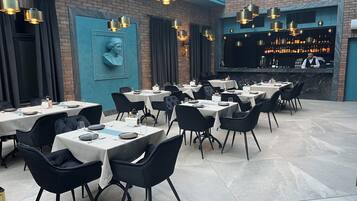 A restaurant with multiple tables and chairs, a bar area, and a mural on the wall.