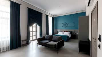 Una habitación de hotel moderna con sofá, cama con ropa de cama azul, una mesita y un armario.
